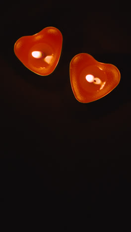 Vertical-Video-Of-Two-Romantic-Lit-Heart-Shaped-Red-Candles-On-Black-Background-With-Copy-Space